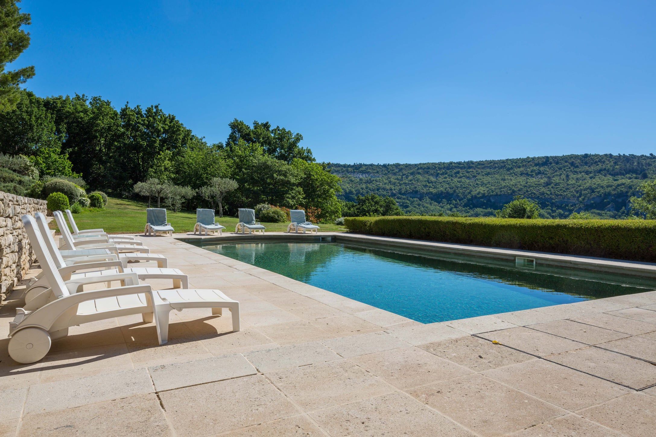 Sun loungers beside the heated pool, looking out over wooded hills