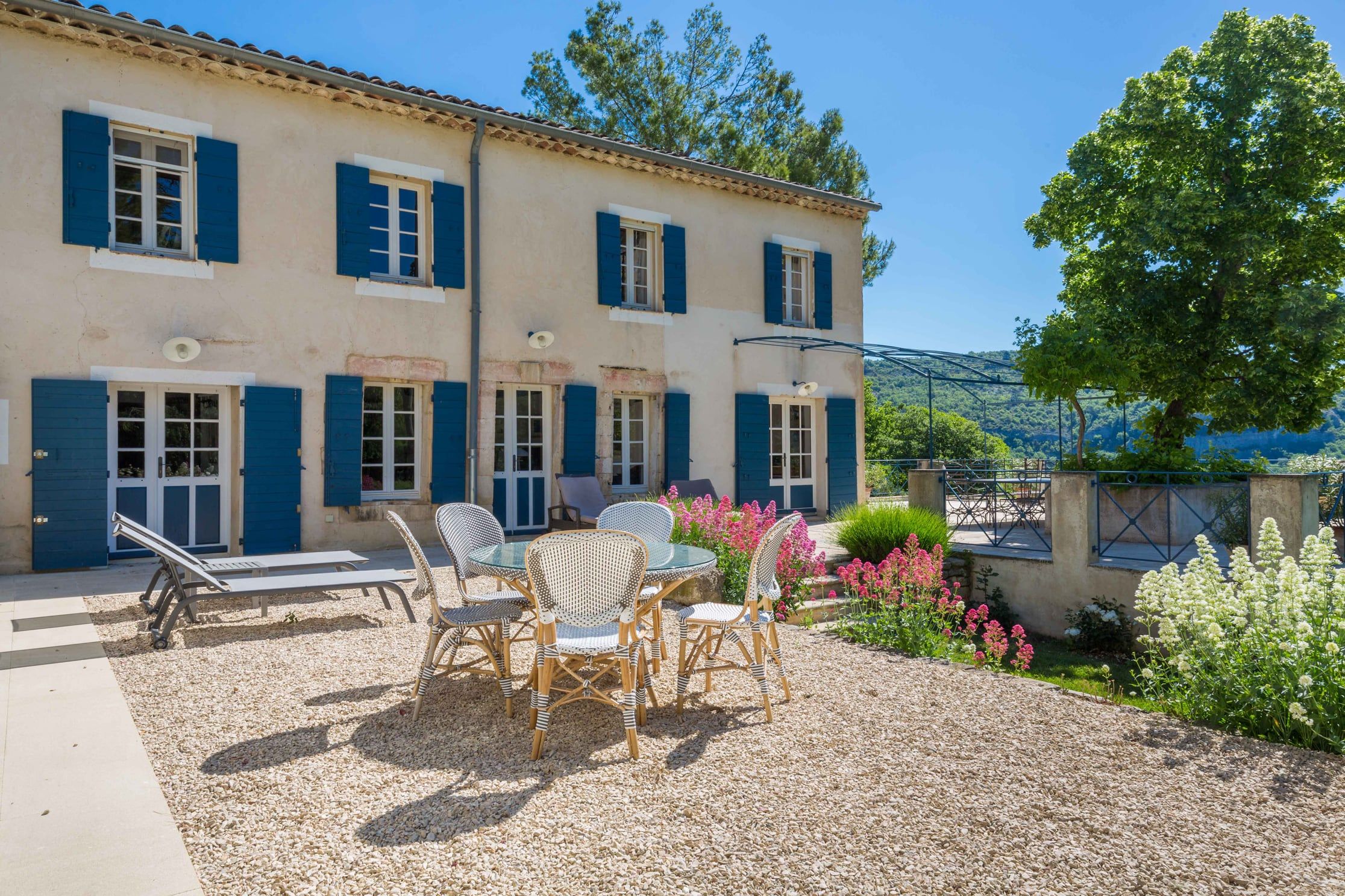Tables and chairs on the terrace in front of the blue-shuttered stone farmhouse